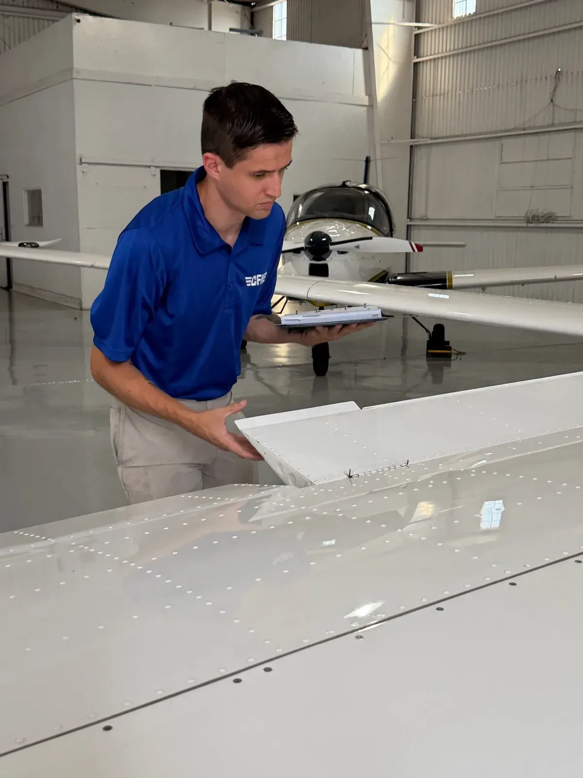 A student checking the wing of a P-Mentor against his checklist in the hangar