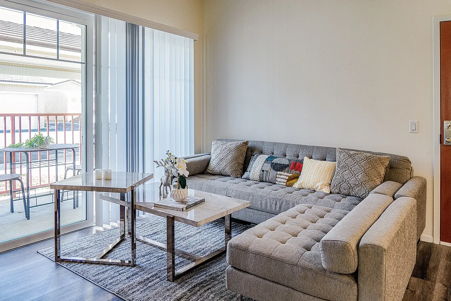 An apartment living room with a sectional sofa and a sliding door onto a private balcony