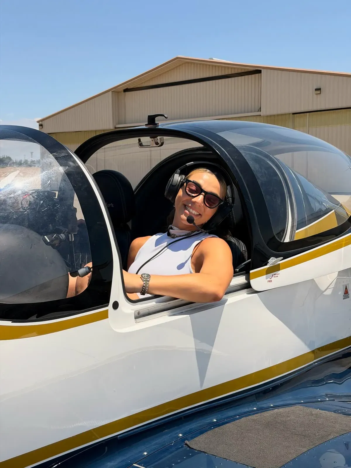 A smiling student wearing a headset in the cockpit, canopy open